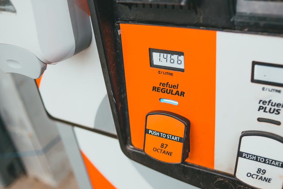 Close-up image of a fuel pump at a gas station, displaying a digital screen that reads 1.4466 litres, with a bright orange and white design. The pump has a black and orange button labeled 'Push to Sta